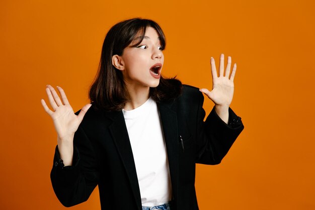 オレンジ色の背景で隔離の黒いジャケットを着て怖い若い美しい女性