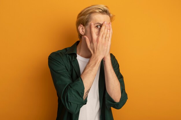 Scared young blonde guy wearing green t-shirt covered face with hands