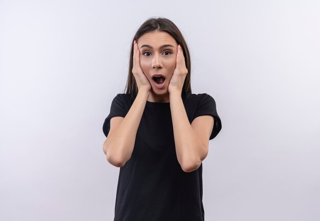 Scared young caucasian girl wearing black t-shirt put her hands on cheek on isolated white background