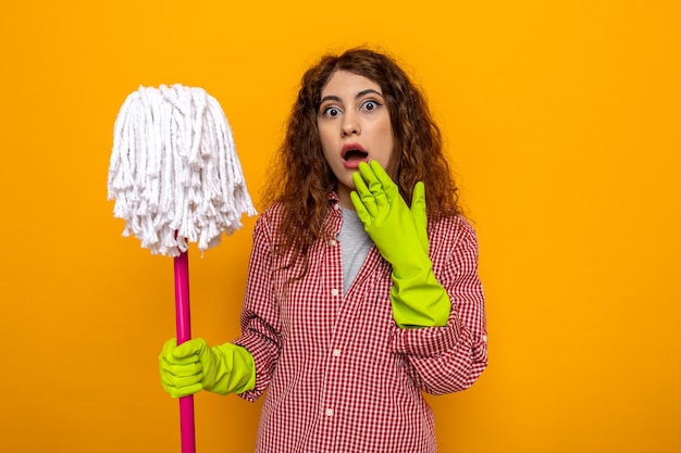 Scared young cleaning woman wearing gloves holding mop 