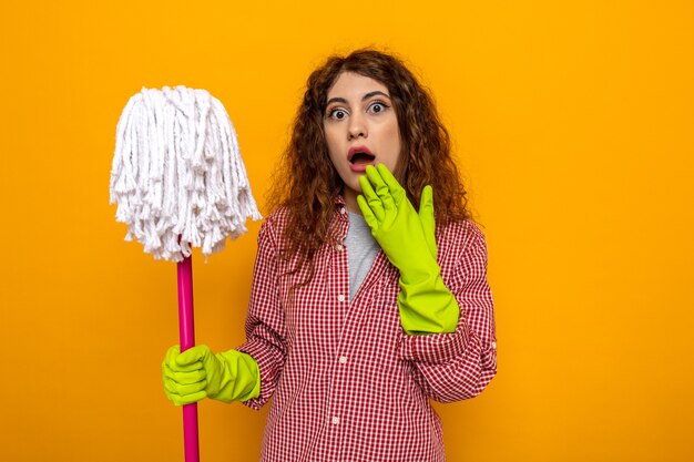 Испуганная молодая уборщица в перчатках держит швабру