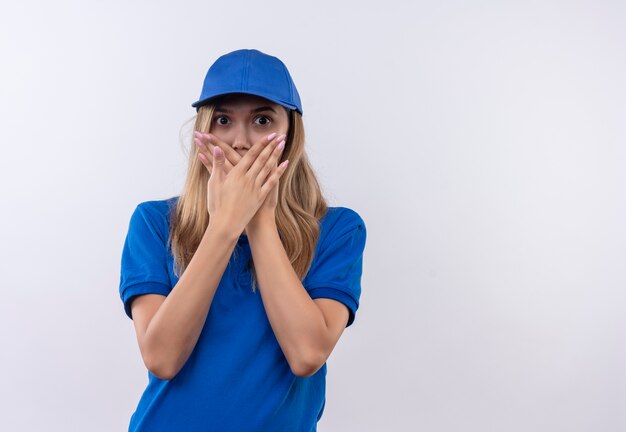 Scared young delivery girl wearing blue uniform and cap covered mouth with hands isolated on white