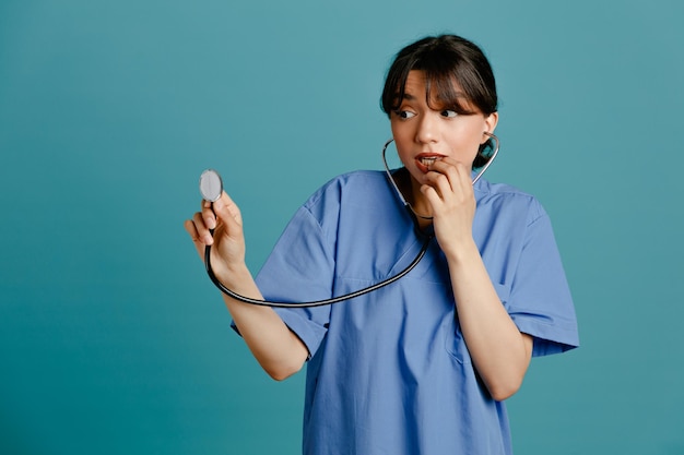 Free photo scared young female doctor wearing uniform fith stethoscope isolated on blue background