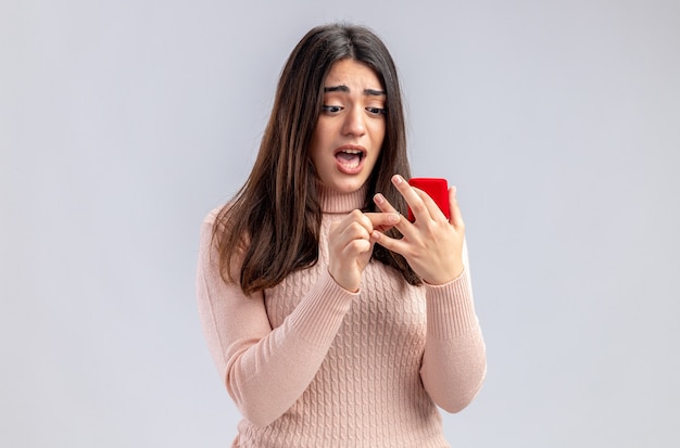 Scared young girl on valentines day holding and looking at wedding ring isolated on white background