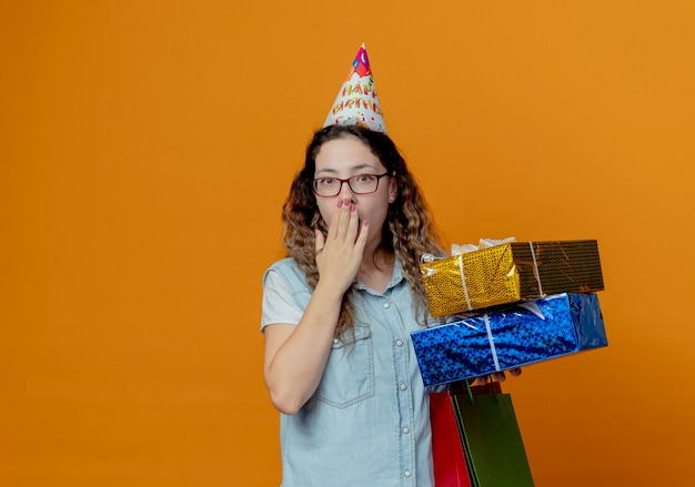 Foto gratuita ragazza spaventata con gli occhiali e berretto di compleanno che tiene scatole regalo con sacchetti regalo