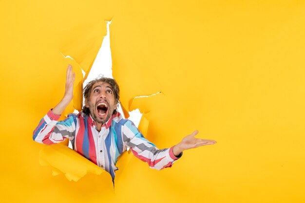 Scared young guy looking up in torn yellow paper hole background