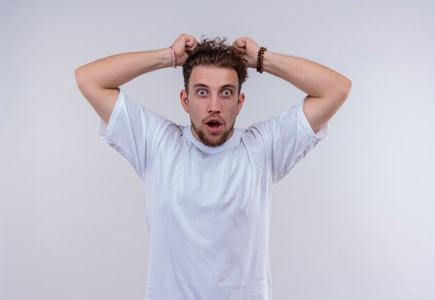 Scared young guy wearing white t-shirt grabbed hair on isolated white background