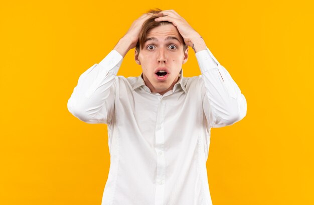 Scared young handsome guy wearing white shirt grabbed head isolated on orange wall