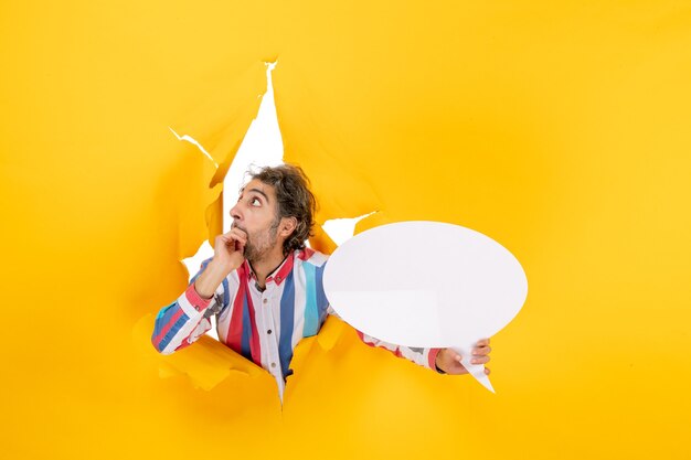 Scared young man pointing white page with free space in a torn hole in yellow paper