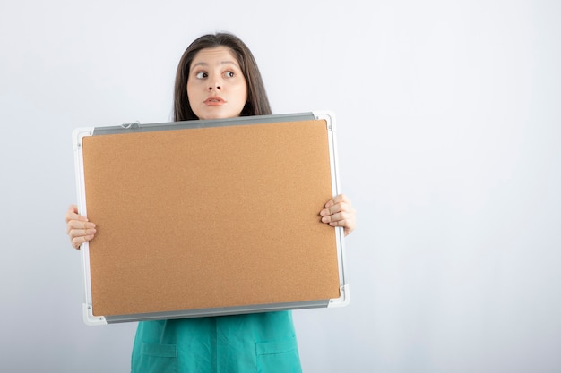 Scared young nurse looking away while holding board.