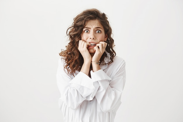 Free photo scared young woman biting fingernails, shivering from fear