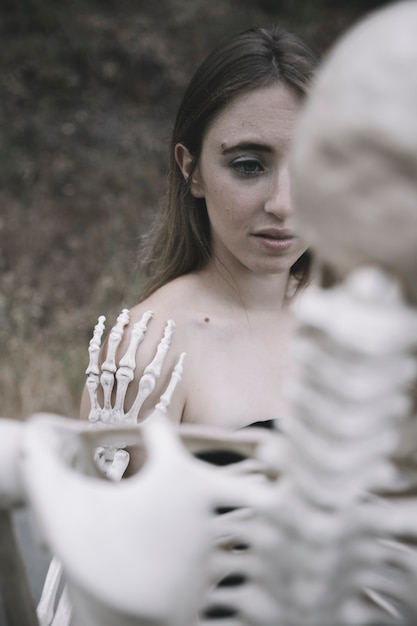 Scared young woman behind skeleton