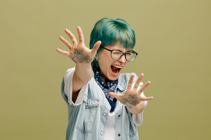 무료 Photo 겁에 질린 젊은 여성이 목에 안경 반다나를 두르고 한쪽 눈을 감고 카메라를 향해 손을 뻗어 올리브 녹색 배경에 격리된 제스처를 보여주지 않습니다