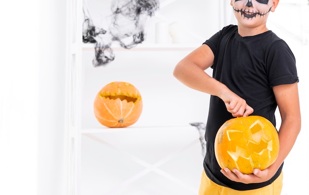 Free photo scary boy holding carved pumpkin for halloween