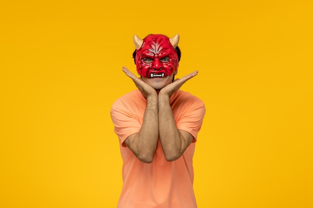 Scary mask young terrifying guy making cute face with hands on chin wearing scary red mask