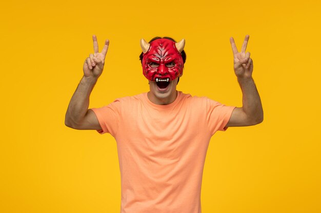 Scary mask young terrifying guy making peace sign with open mouth