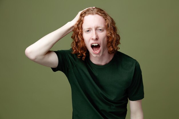 Scary putting hand on head young handsome guy wearing green t shirt isolated on green background