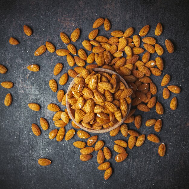 Scattered almonds in a bowl on a grungy grey table. top view.