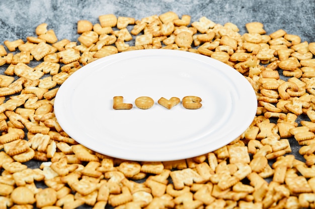 Scattered alphabet crackers and word love spelled with crackers on a white plate.