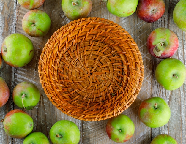 Scattered apples with empty basket on wood