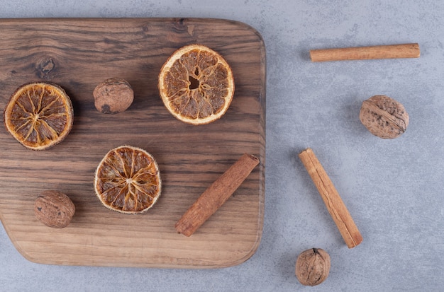 Scattered bundle of dried lemon slices, cinnamon sticks and walnuts on marble surface