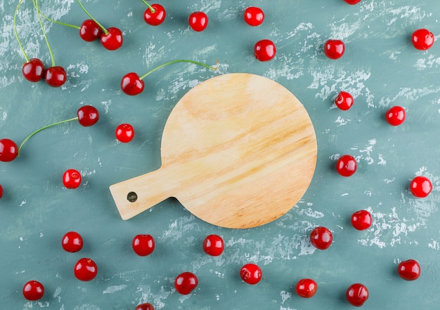 Scattered cherries on plaster and cutting board, flat lay.