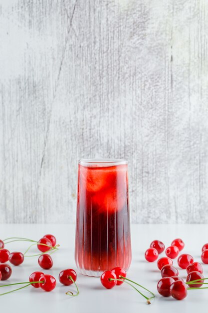 Scattered cherries with icy drink side view on white and grungy table