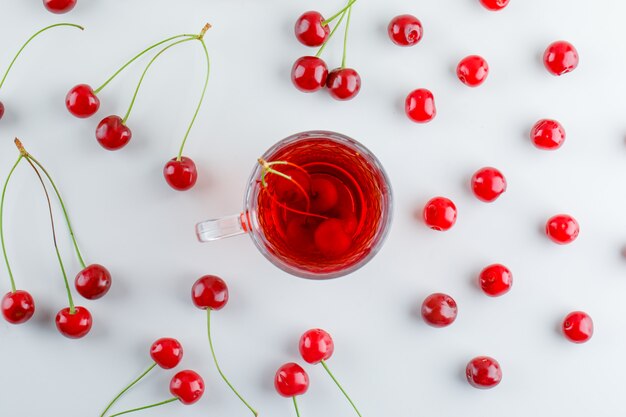 Scattered cherries with tea, flat lay.