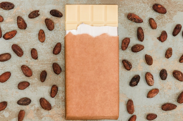 Scattered cocoa beans with white chocolate bar on grunge background
