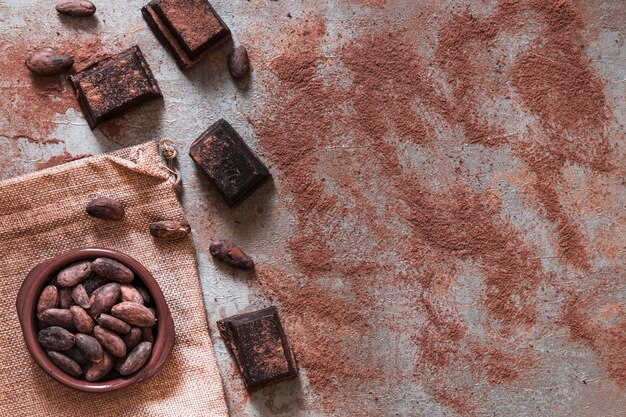 Scattered cocoa powder with chocolate pieces and cocoa beans bowl