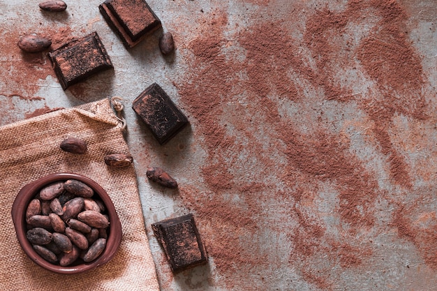 Scattered cocoa powder with chocolate pieces and cocoa beans bowl