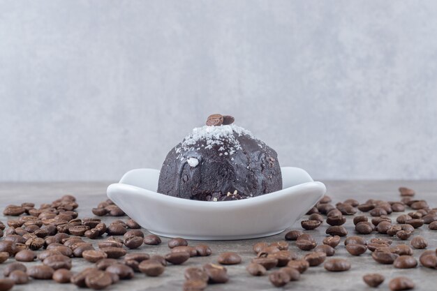 Foto gratuita chicchi di caffè sparsi intorno a un piccolo piatto con una torta ricoperta di cioccolato su una superficie di marmo