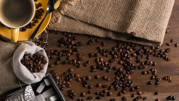 Scattered coffee beans near cup, box of sugar and sackcloth