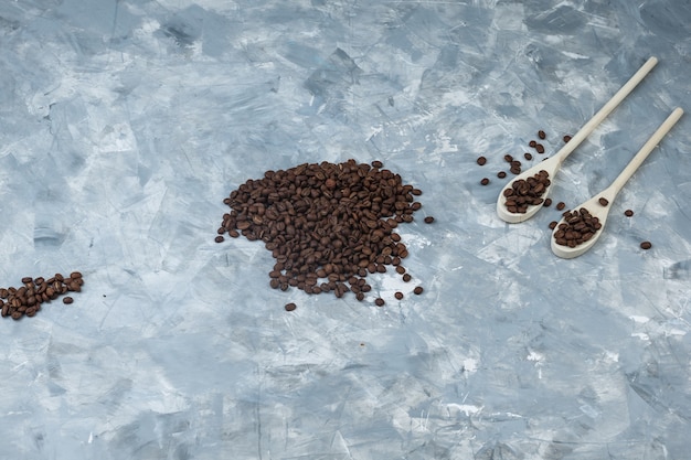 Scattered coffee beans in wooden spoons on a grey plaster background. flat lay.