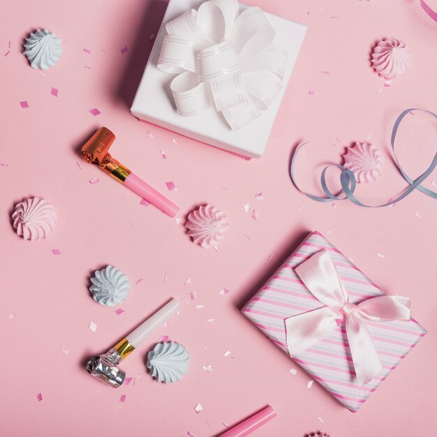 Scattered confetti; whipped cream and party blower with gift boxes on pink backdrop