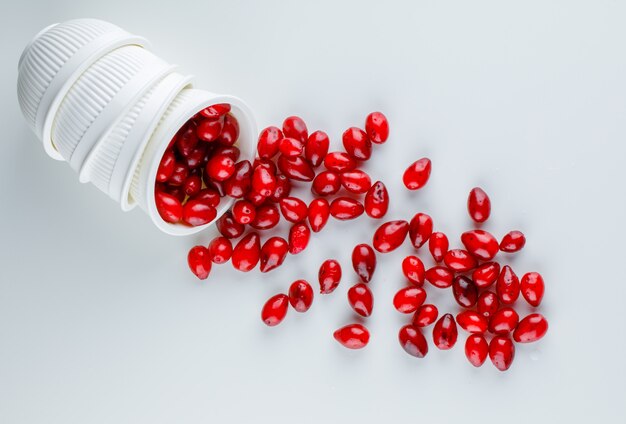 Scattered cornel berries from a bowl on white. flat lay.