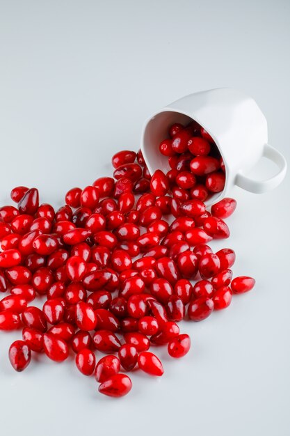 Scattered cornel berries from a cup on white. high angle view.