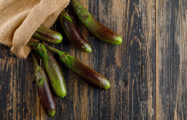 Scattered eggplants from a burlap sack flat lay on a wooden