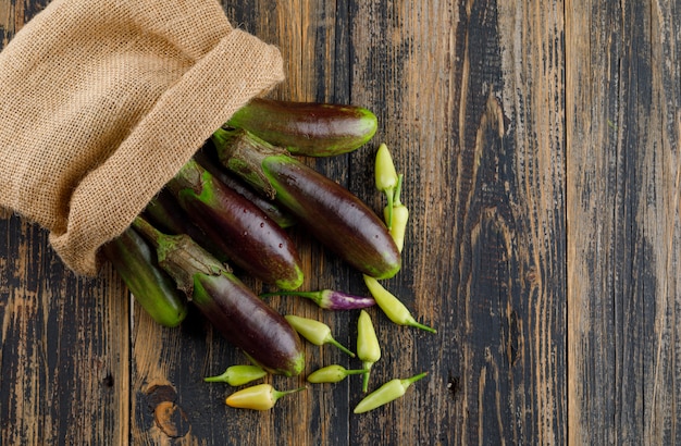 Scattered eggplants with peppers from a burlap sack on wooden,