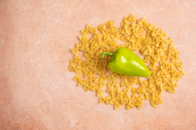 Scattered farfalle pasta with green pepper on orange.