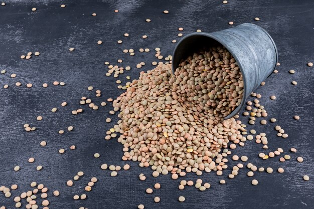 Scattered green lentils in a black mini bucket on a black stone table. high angle view.