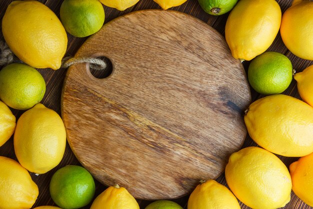 Scattered lemons with limes on wooden and cutting board, flat lay.