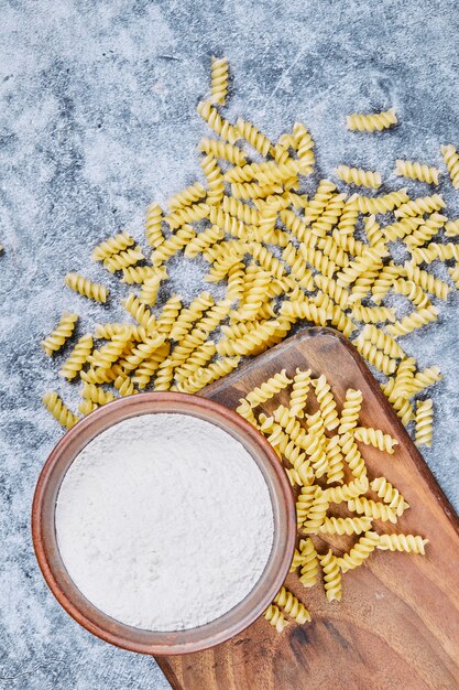 Scattered pasta and bowl of flour on blue background
