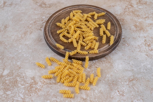 Foto gratuita porzione sparsa di pasta cruda su una tavola di legno e su una superficie di marmo.