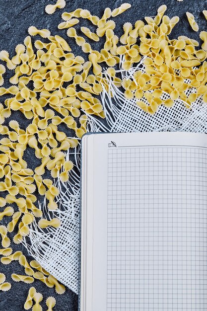Scattered raw pastas around notebook and white tablecloth.