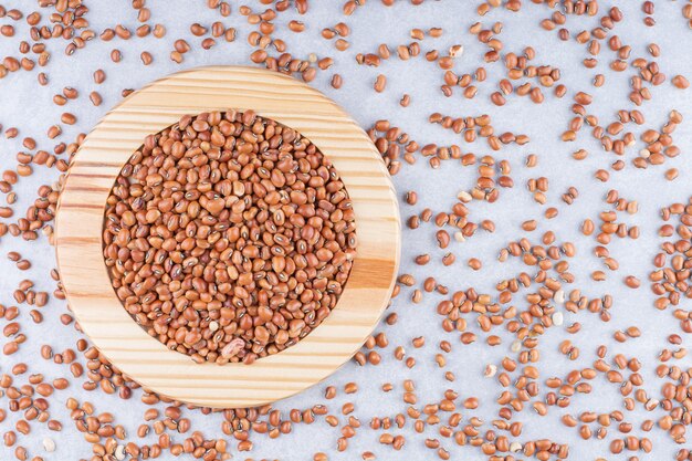 Scattered red beans with a full wooden plate sitting in the middle on marble surface