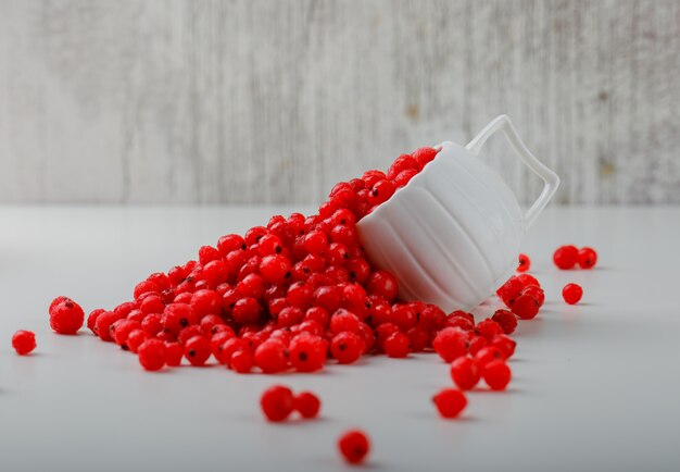 Scattered red currants in a white cup.