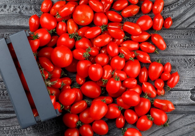 Scattered tomatoes from a wooden box on a grey wooden wall. top view.