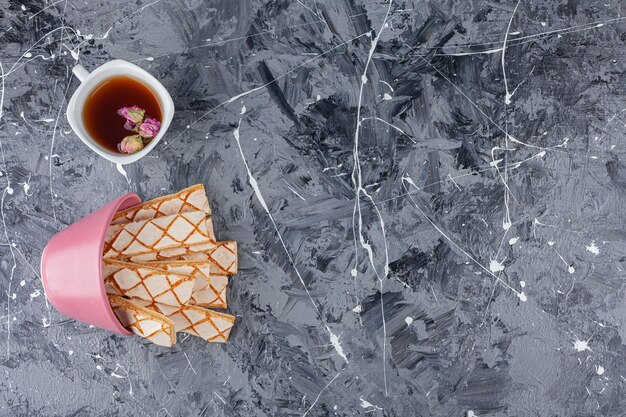 Scattered waffle cookies with a cup of herbal tea .