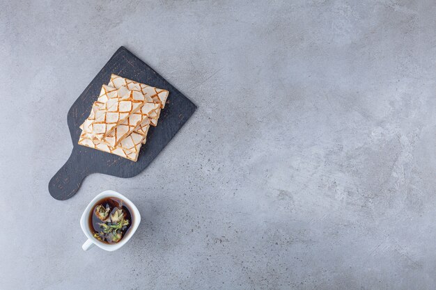 Scattered waffle cookies with a cup of herbal tea .